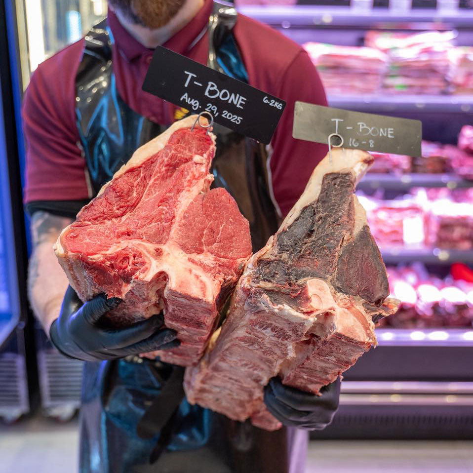 Person holding two large cuts of meat with tags in a grocery store setting
